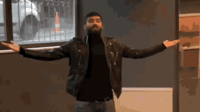 a man with a beard wearing a leather jacket is standing with his arms outstretched