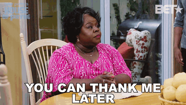 a woman in a pink shirt sits at a table with the words you can thank me later below her