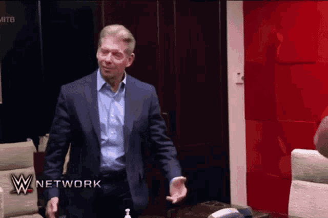 a man in a suit is standing in front of a red wall with the words w network on it .