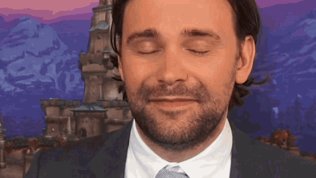 a man in a suit and tie with his eyes closed and a castle in the background