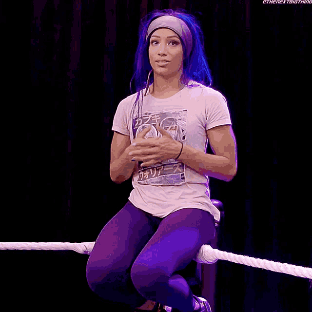 a woman with blue hair is sitting on a rope in a wrestling ring