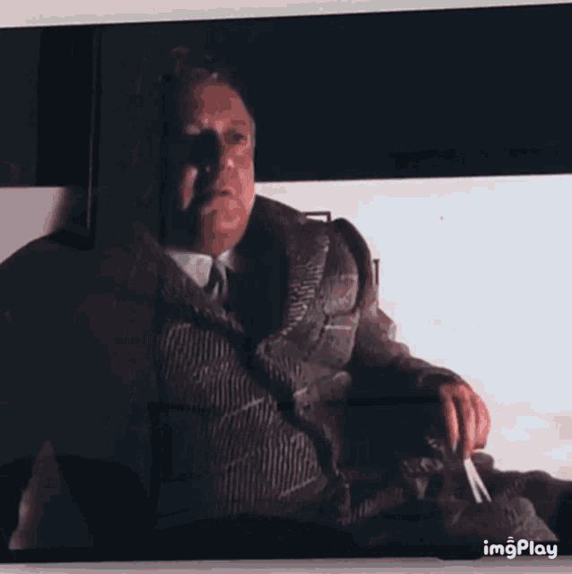 a man in a suit and tie is sitting on a couch smoking a cigarette