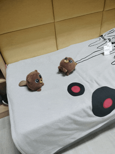 two stuffed animals are laying on a bed with a blanket that has a drawing of a bear on it