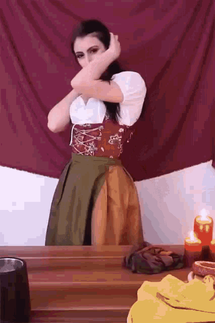 a woman in a costume is standing in front of a table with candles and a red cloth .