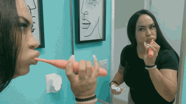 a woman is brushing her teeth in front of a mirror with a picture of a face on the wall