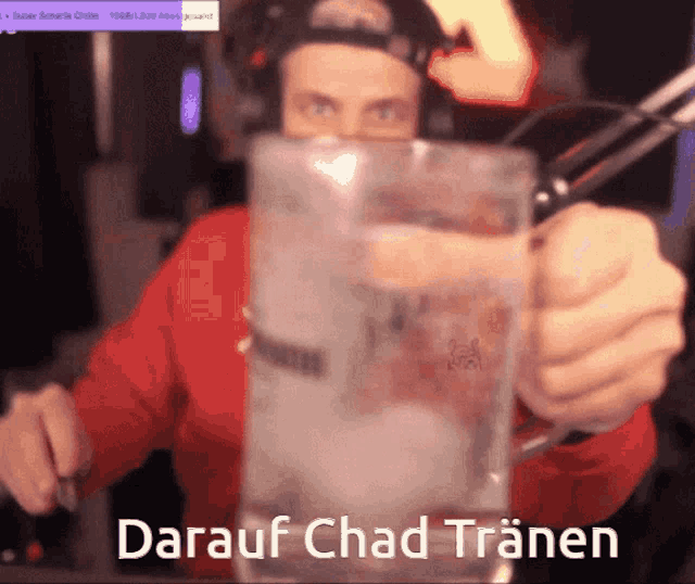 a man in a red shirt is holding a large glass of water with the words " darauf chad tränen " written on it
