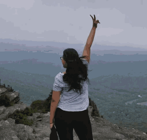 a woman stands on top of a mountain with her arm up in the air