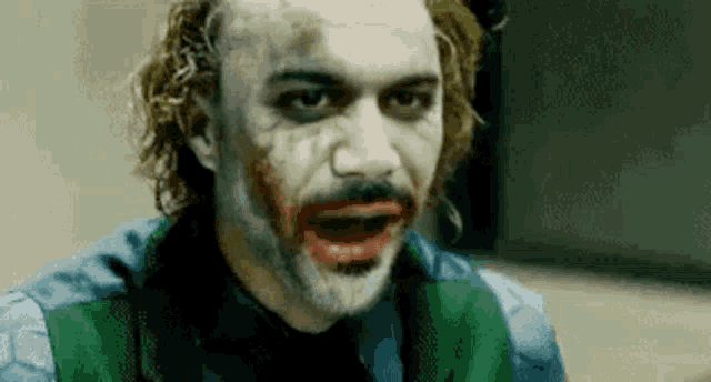 a close up of a man in a joker costume with a beard and red lipstick on his face .
