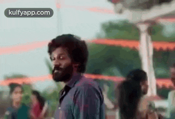 a man with a beard is standing in front of a crowd of people in a park .