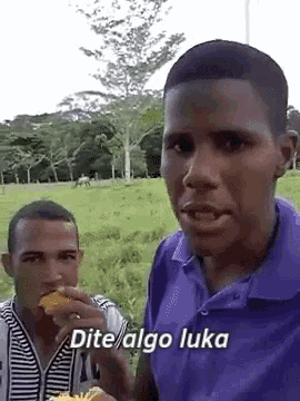 a man in a purple shirt says " dite algo luka " while eating food