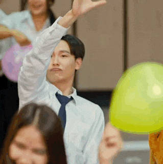 a man in a tie is holding a yellow balloon in his hand while sitting in front of a group of people .