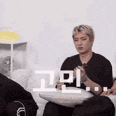 a man in a black shirt is sitting on a couch with a pillow in his lap .