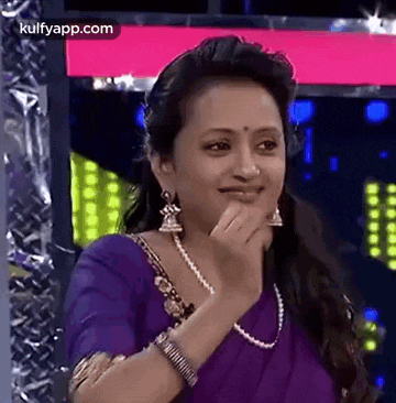 a woman in a purple saree and pearls is smiling and covering her mouth .