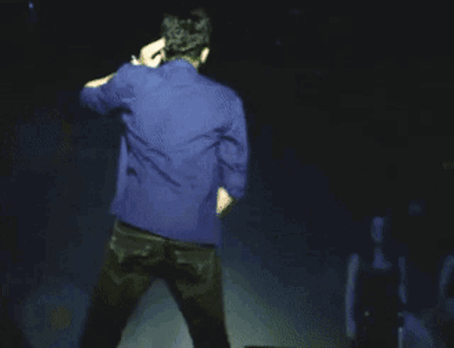 a man in a blue jacket is dancing on stage