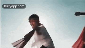 a man in a white cape is flying through the air while a woman in a red dress is standing behind him .