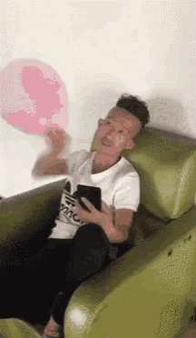 a man is sitting in a chair holding a pink balloon and using a cell phone .