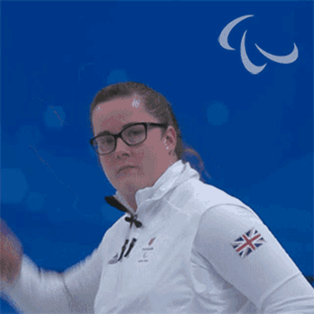 a woman wearing glasses and a white jacket with a british flag on the sleeve