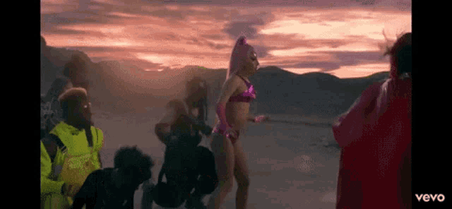 a woman in a pink bikini is dancing in the desert with other people