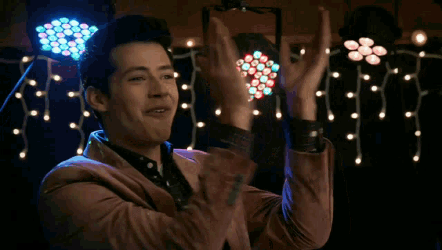 a man in a brown jacket is clapping his hands in front of a bunch of lights