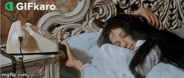 a woman is sleeping in a bed next to a telephone on a nightstand .