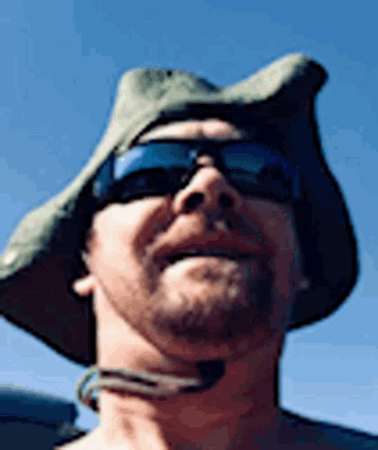 a man wearing a hat and sunglasses is looking up at the camera .