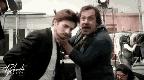a man in a suit and tie is being held by another man with the name roberto written on the bottom