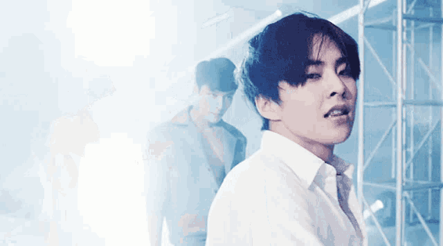 a man in a white shirt looks at the camera with another man behind him
