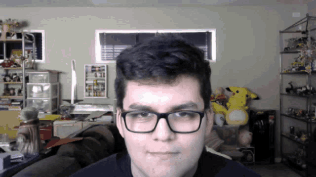 a young man wearing glasses looks at the camera in a room filled with stuffed animals