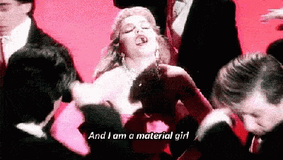a woman in a red dress is dancing in front of a crowd of people and says `` and i am a material girl '' .