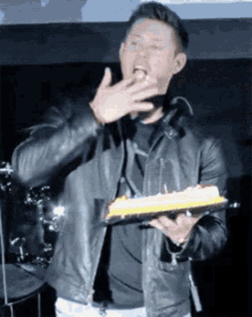 a man in a leather jacket is holding a cake with candles on it .