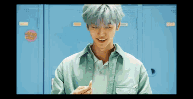 a young man with gray hair is standing in front of blue lockers .