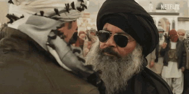 a man with a beard and sunglasses is standing next to another man in a crowd .