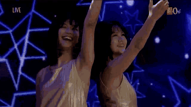 two women are standing next to each other with their arms in the air .