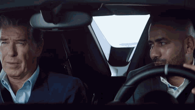 a man in a suit sits next to a man in a suit in a car