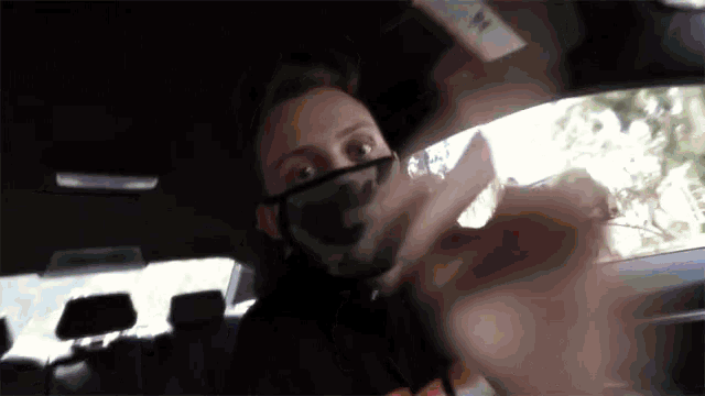 a man wearing a face mask is sitting in a car and giving the middle finger