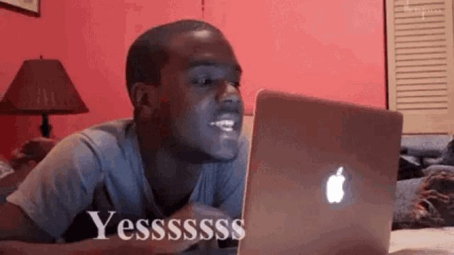 a man is sitting in front of an apple laptop and smiling .