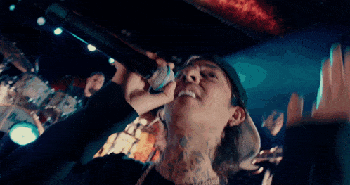 a man with a tattoo on his neck is singing into a microphone in front of a crowd