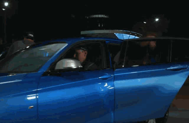 a man with a beard is getting out of a blue bmw