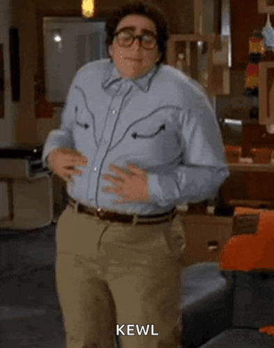 a man in a blue shirt and khaki pants is dancing in a living room while wearing glasses .