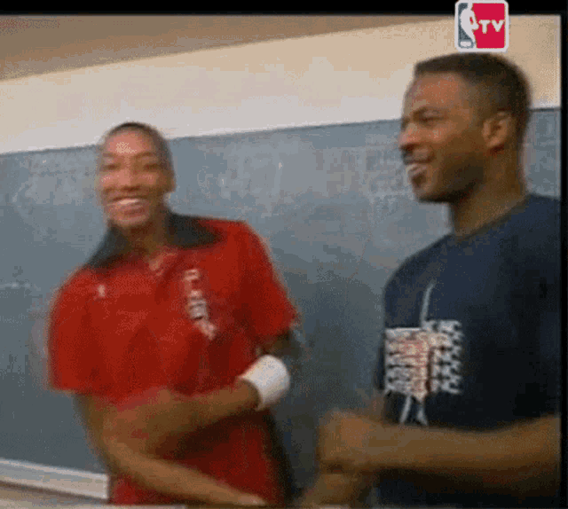 two men are standing next to each other in front of a blackboard with a nba tv logo in the corner .