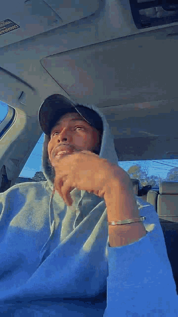 a man wearing a blue hoodie and a black hat is sitting in a car