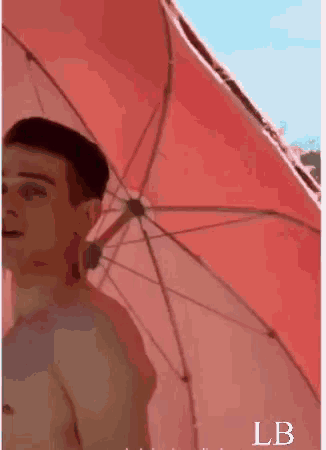 a man without a shirt is standing under a red umbrella with the letter lb below him