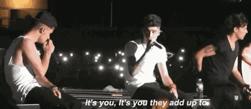 a man singing into a microphone with the words it 's you it 's you they add up to behind him