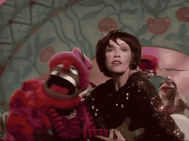 a woman in a sequined dress stands next to a muppet in a pink outfit