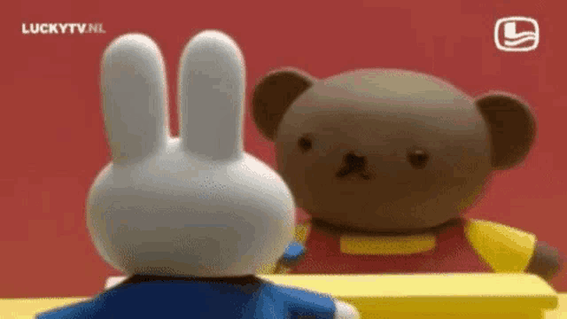 a brown teddy bear and a white rabbit are sitting next to each other .