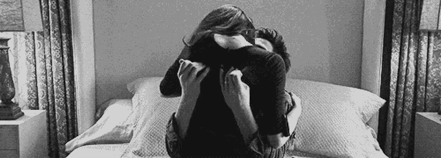 a man and a woman are hugging each other on a bed in a black and white photo .