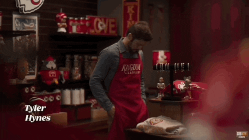 a man wearing a red apron that says kingdom on it is standing in a store .