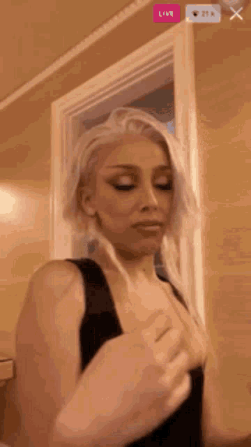 a woman in a black tank top is standing in front of a door and looking at the camera .