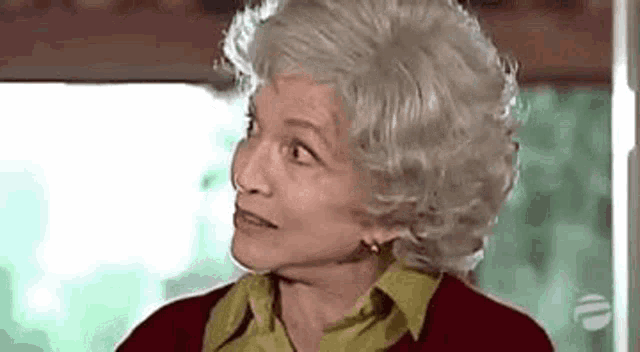 an elderly woman with gray hair and a green shirt is looking at the camera .