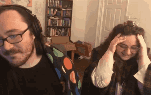 a man wearing headphones stands next to a woman with her hand on her head